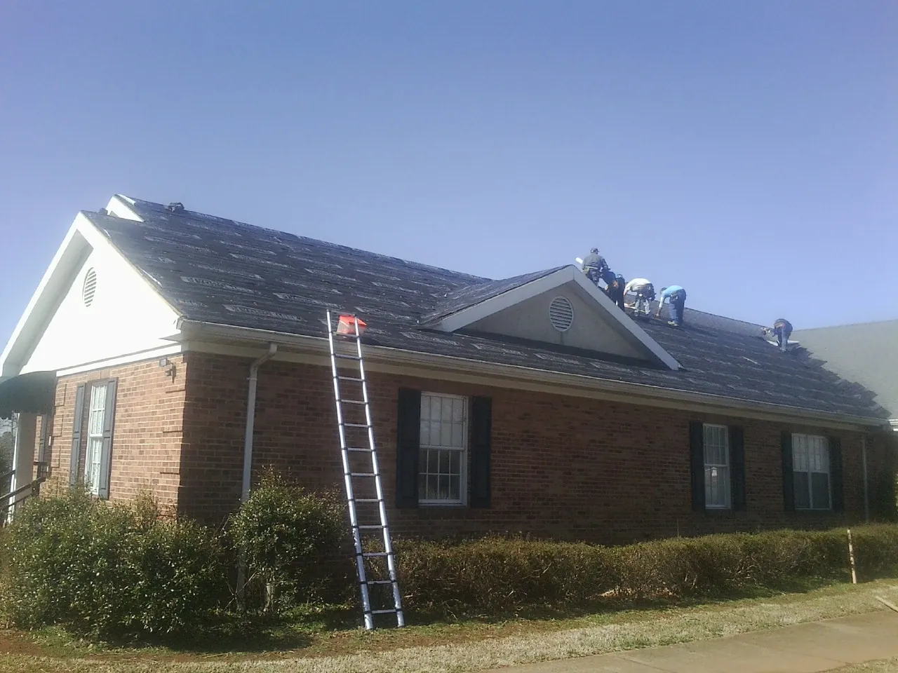 Crew tearing shingles off a brick ranch roof with a ladder set — Emergency Roof Repair work by our crew in Glen Mills