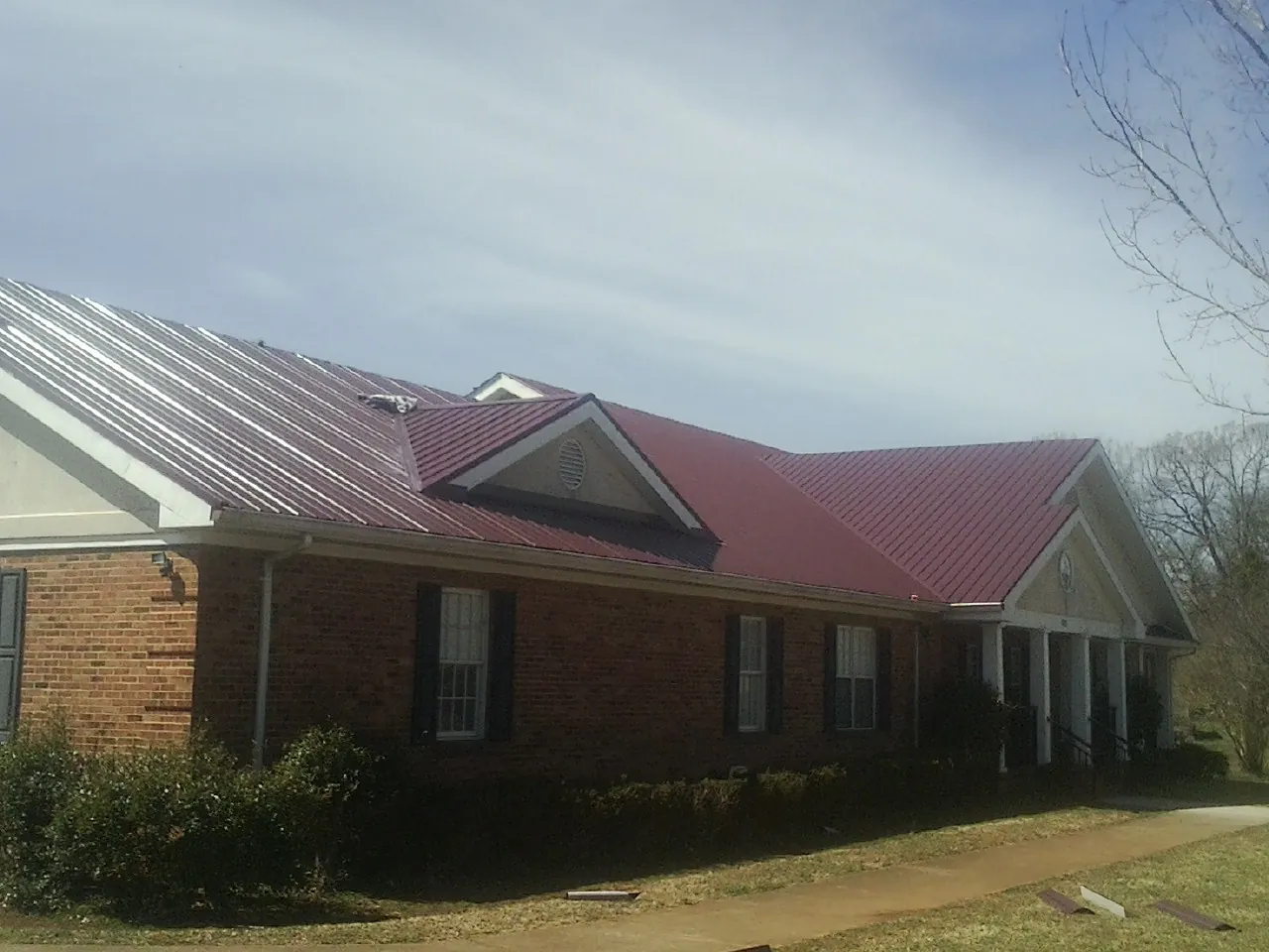 Red metal roof with gabled entries on a long brick building, from a Hail Damage Roof Repair job in Glen Mills