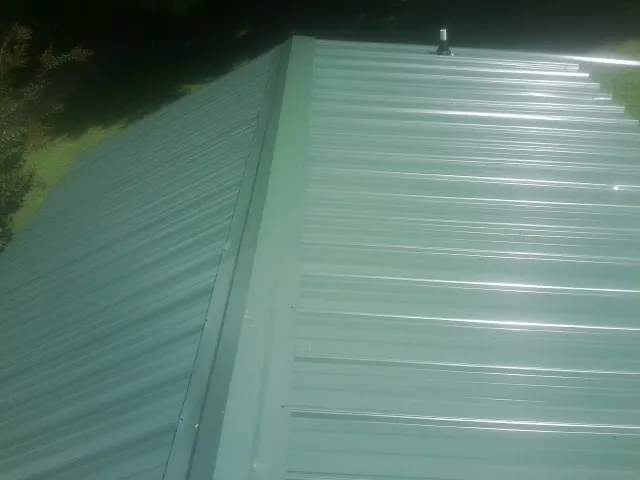 New green metal panels meeting at the ridge of a roof — Flat Roof Repair work by our crew in Glen Mills