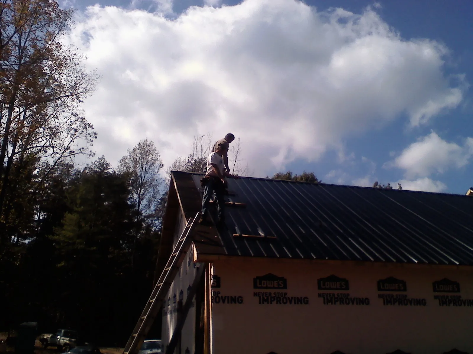 Roofer fastening dark metal panels high against a cloudy sky, from a Roof Inspection job in Glen Mills