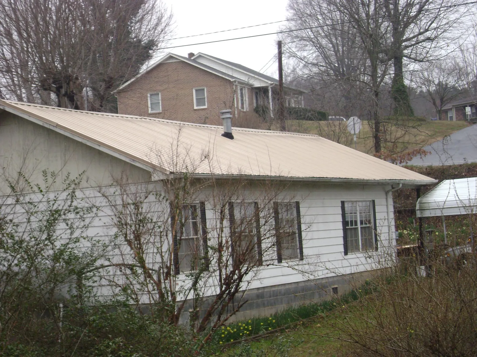 Tan metal roof on a white sided house set into a hillside — Commercial Roofing by Roofing Brothers in Glen Mills