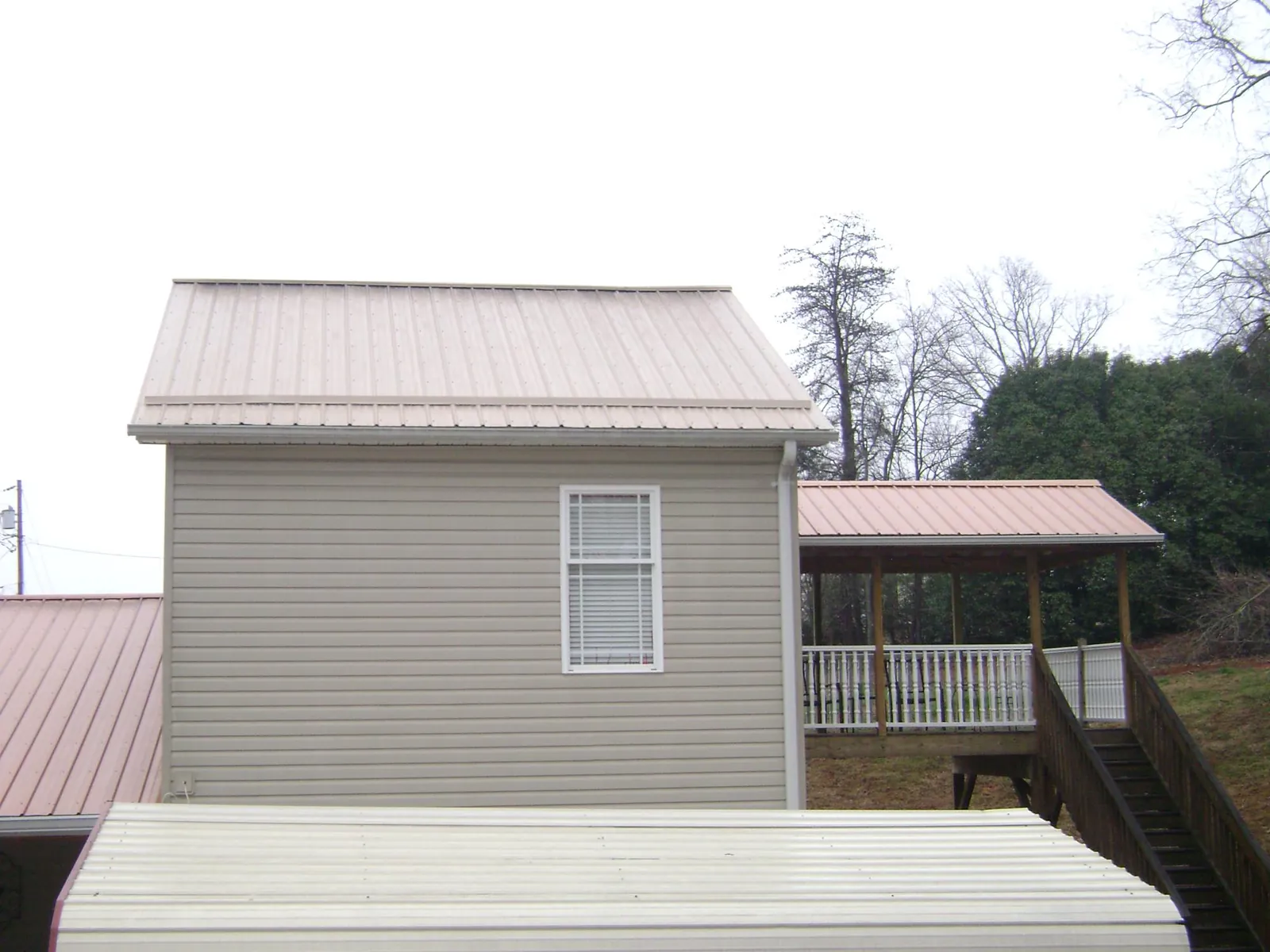 Tan metal roofs on a two story addition and attached porch, from a Roof Replacement job in Glen Mills